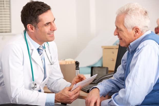 A doctor meeting with an elderly male patient in an exam room.