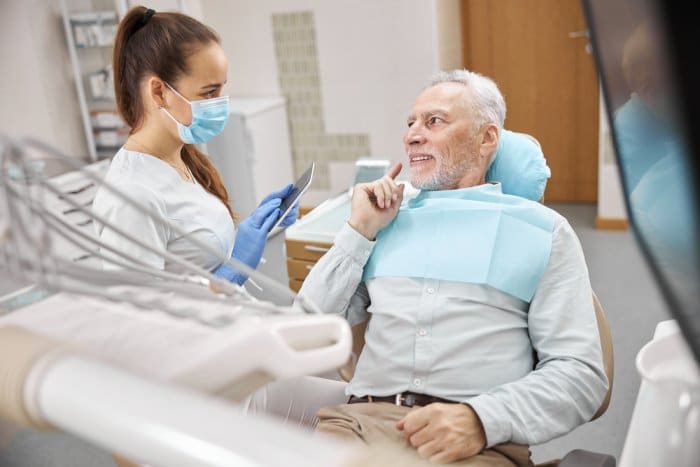 A senior in a dentist chair speaking with the hygienist.