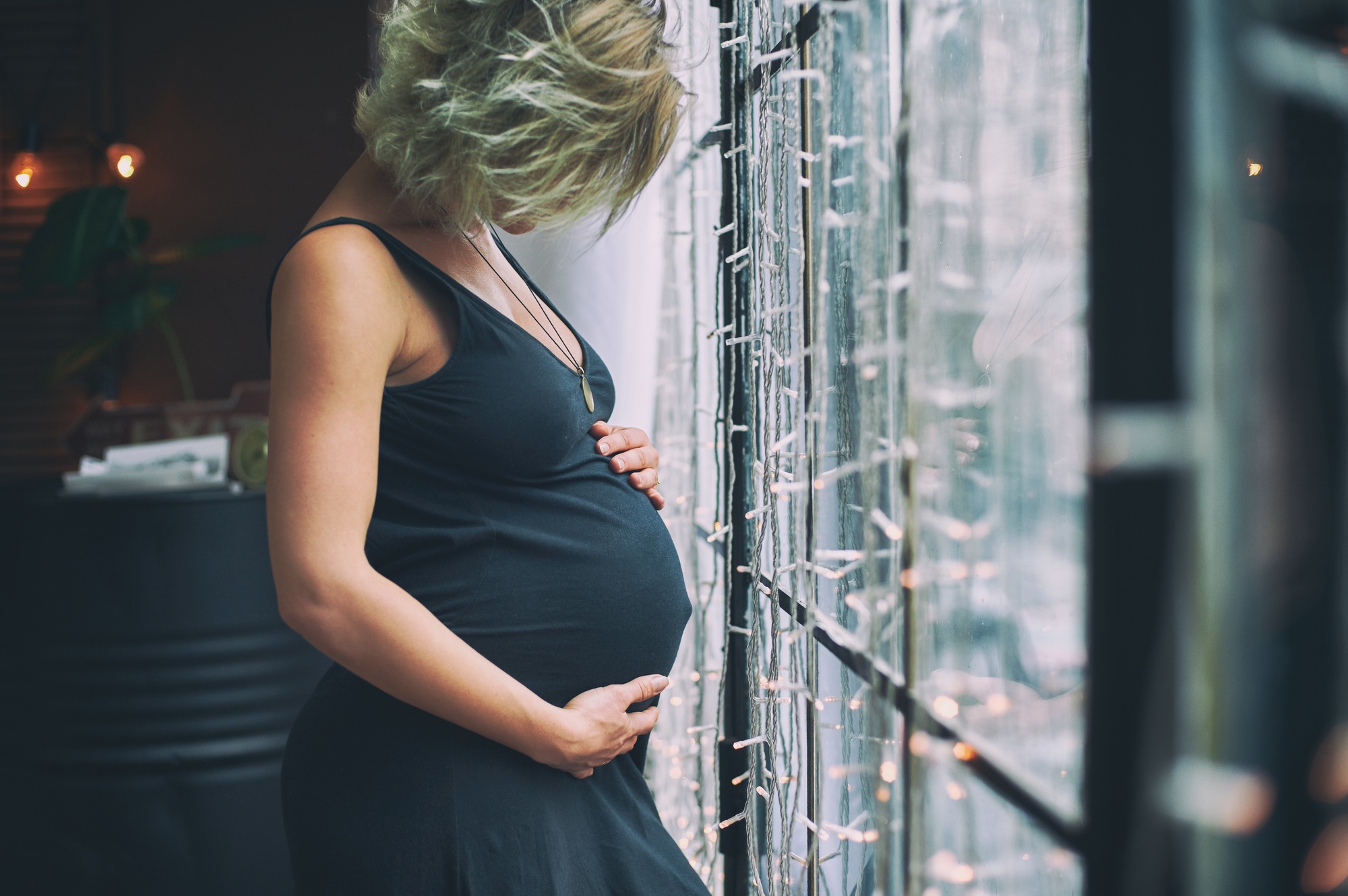 Young beautiful pregnant woman standing near window at loft style home