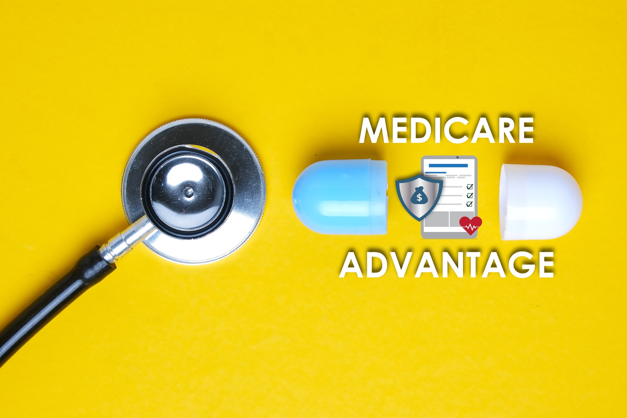 A picture of stethoscope with fake capsule, medicare advantage word, tablet, money shield and heart.