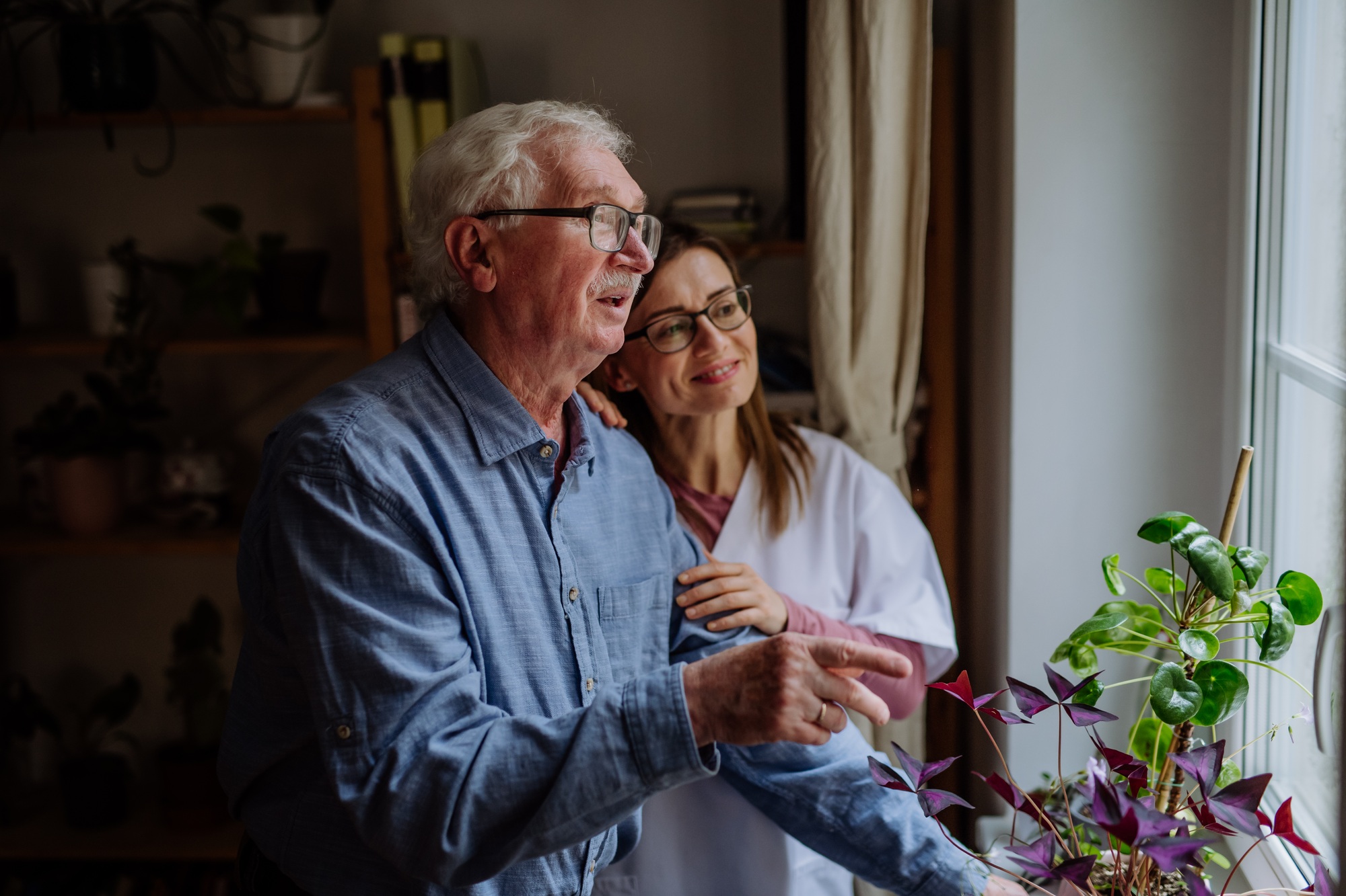 Healthcare worker or caregiver visiting senior man indoors at home, talking.