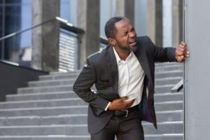 An African-American businessman is standing near the office holding his stomach, severe stomach