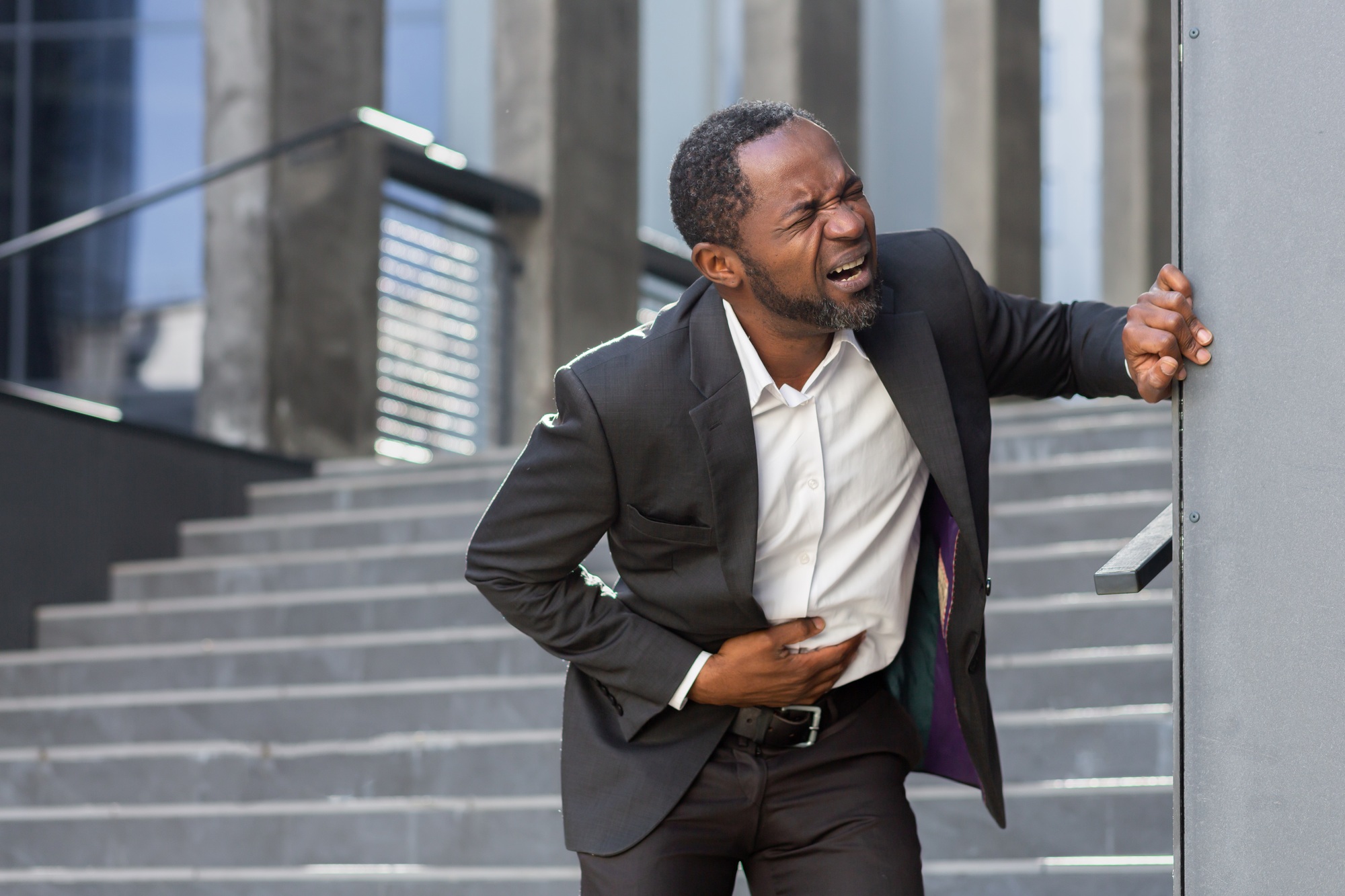 An African-American businessman is standing near the office holding his stomach, severe stomach