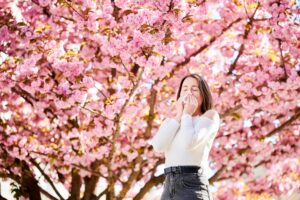 Woman allergic suffering from seasonal allergy at spring, sneezing, blowing nose with handkerchief.